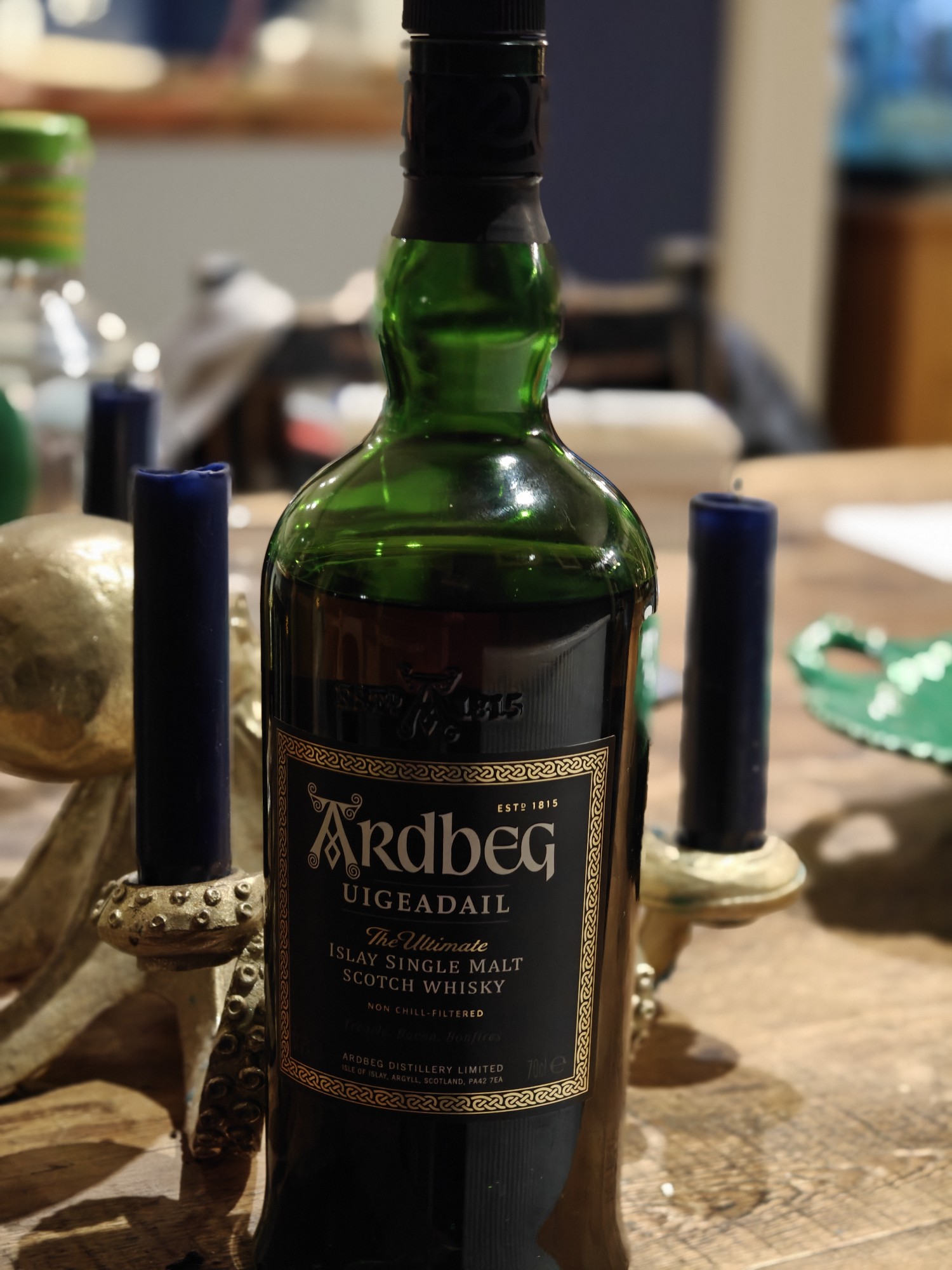 A bottle of scotch whisky - Ardbeg Uigedail - in front of some candles on a table 