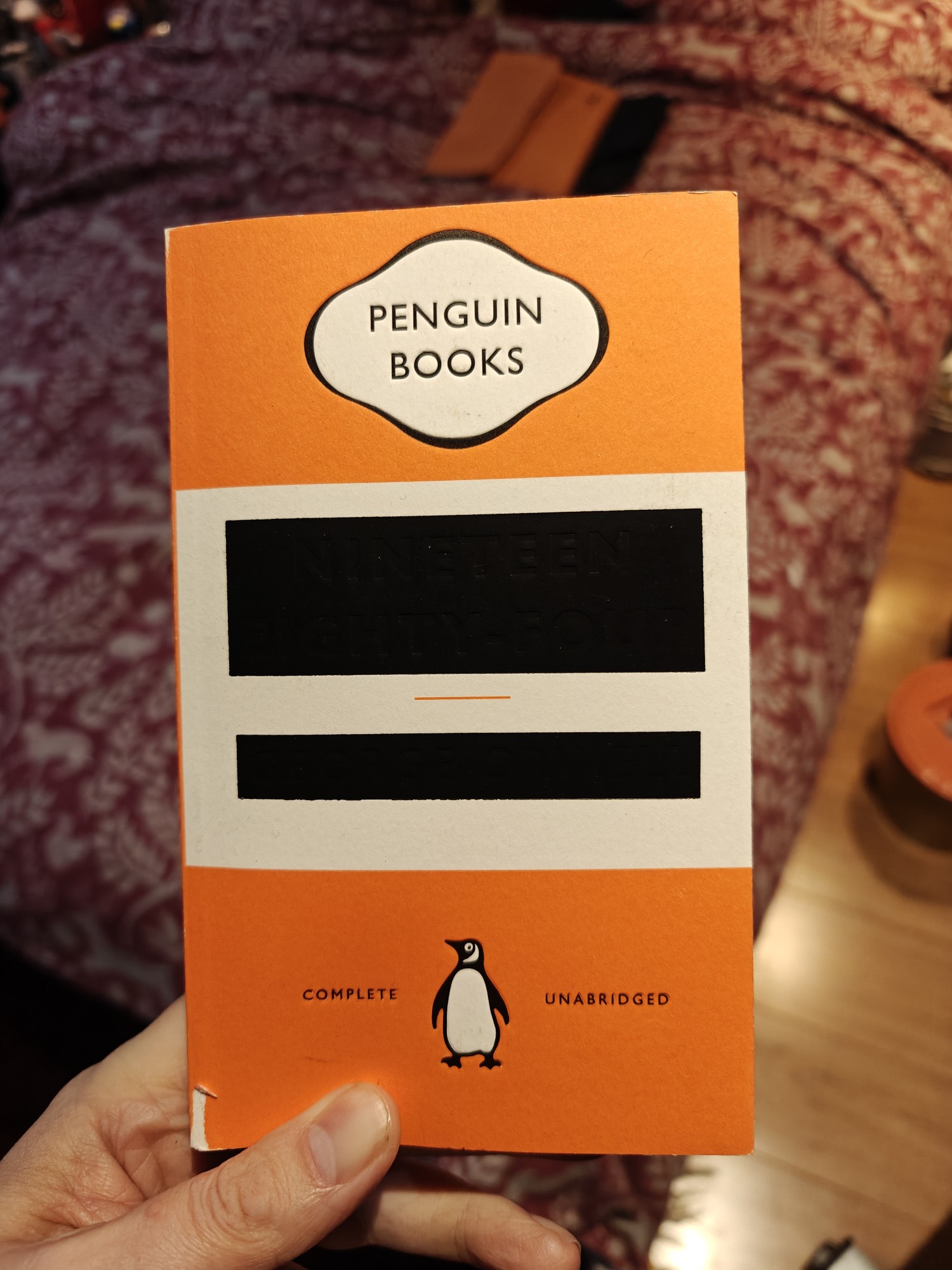 The cover of the Penguin paperback of Nineteen Eighty-Four. It is orange with the Penguin Books logo at the top. The title and author though are blocked out with black boxes to give the effect of censorship. At the bottom is a penguin. 