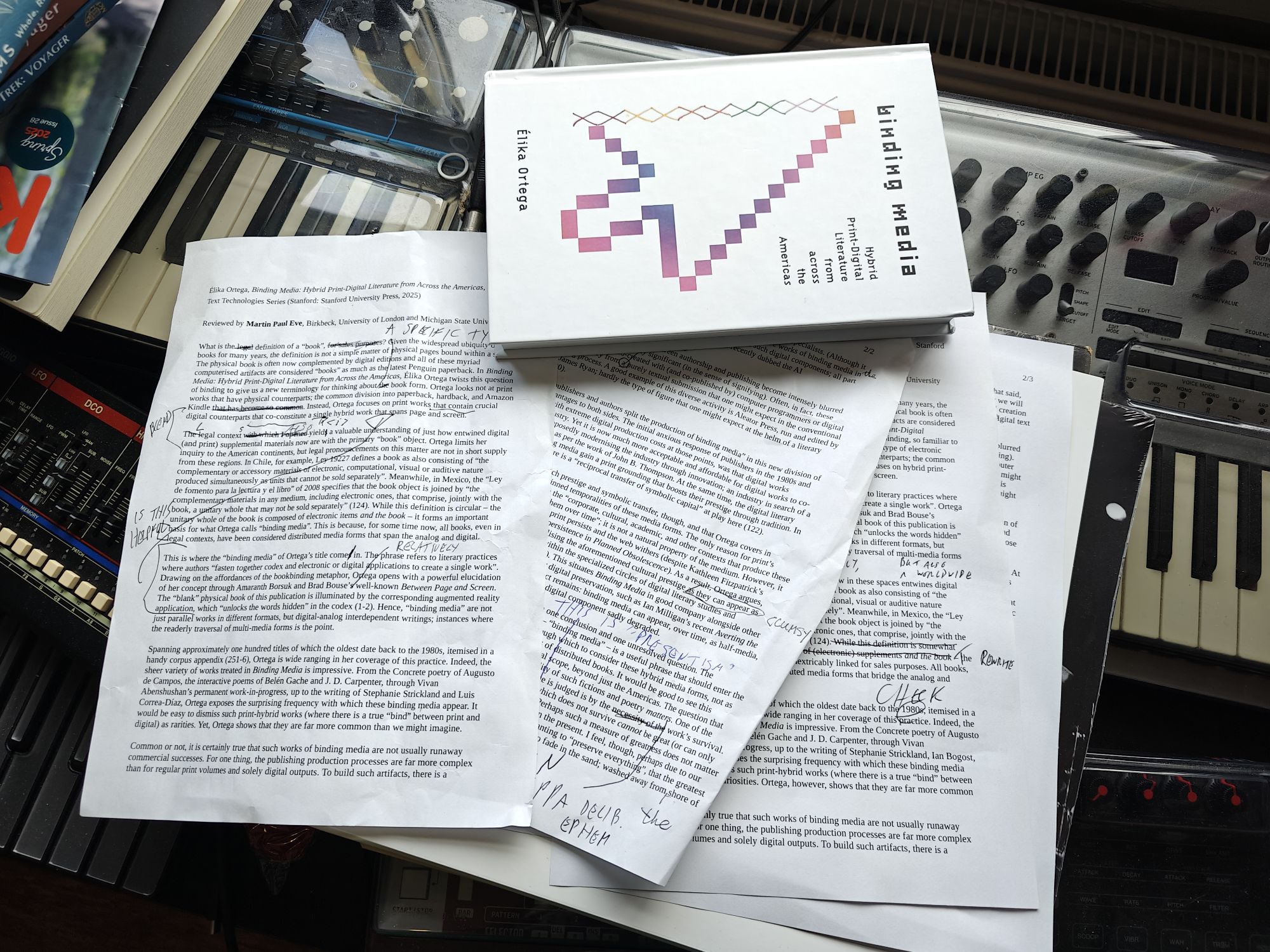 A copy of Elika Ortega's book, Binding Media, atop a stack of printed pages with handwritten scribbled notes and amendments over them 