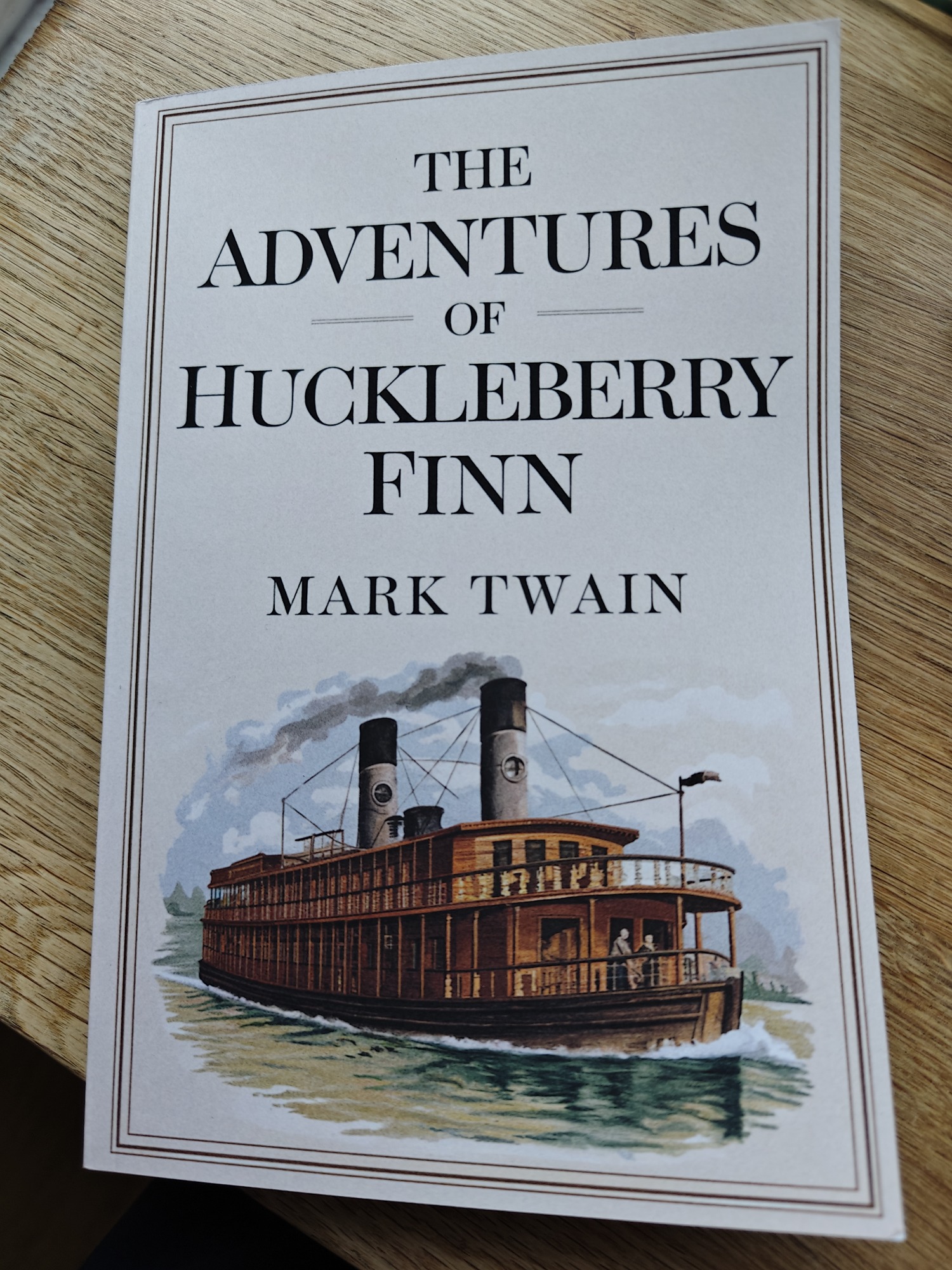 The cover of The Adventures of Huckleberry Finn. Shows a drawing of a river paddle boat. 