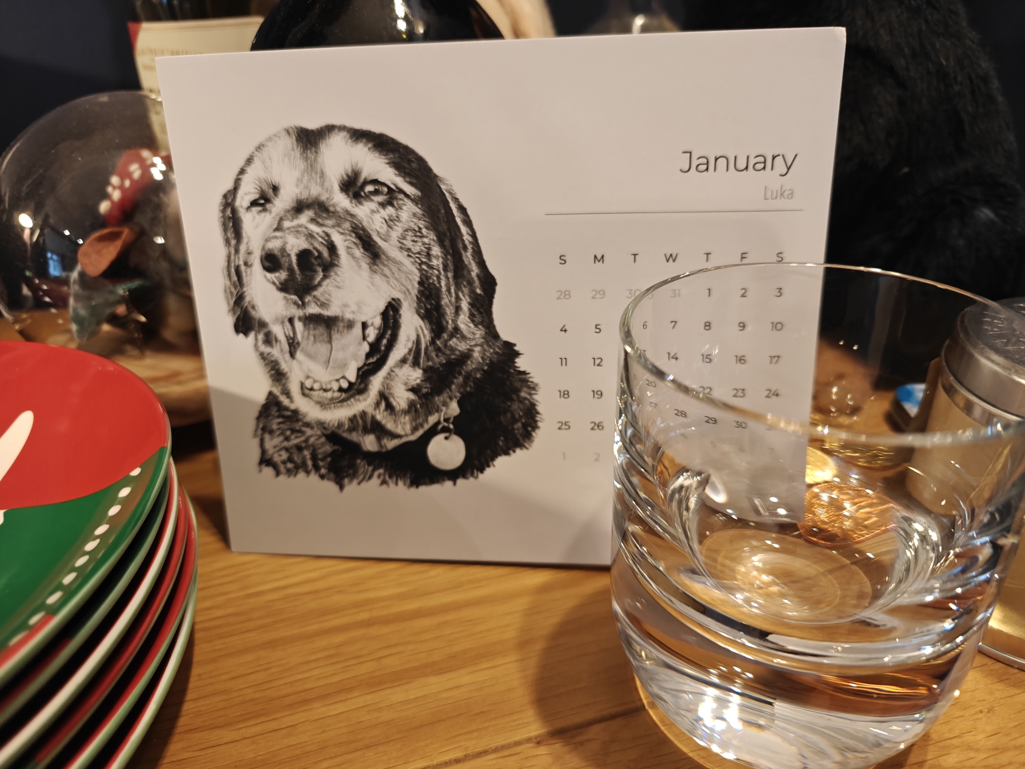 A drawing of a black dog with a whiskey glass in foreground 
